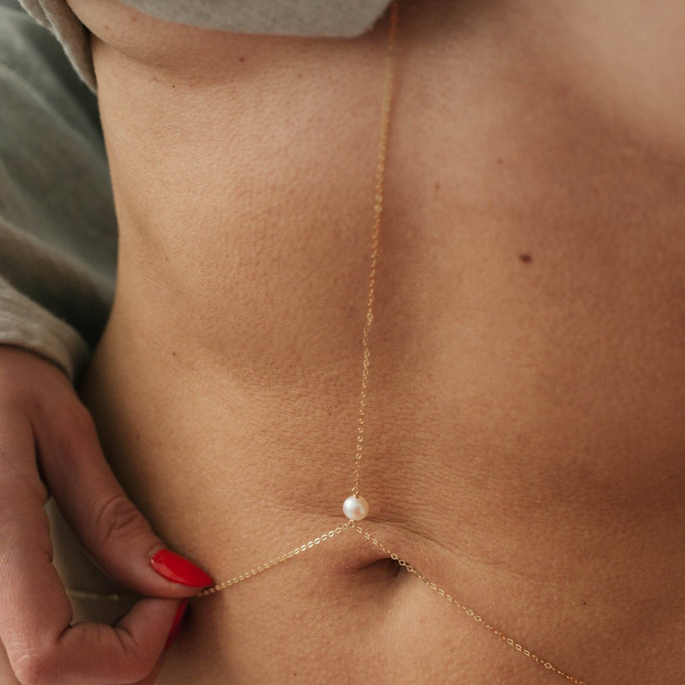 
                      
                        Gold-filled body chain necklace with a round white pearl on a woman's midriff.
                      
                    