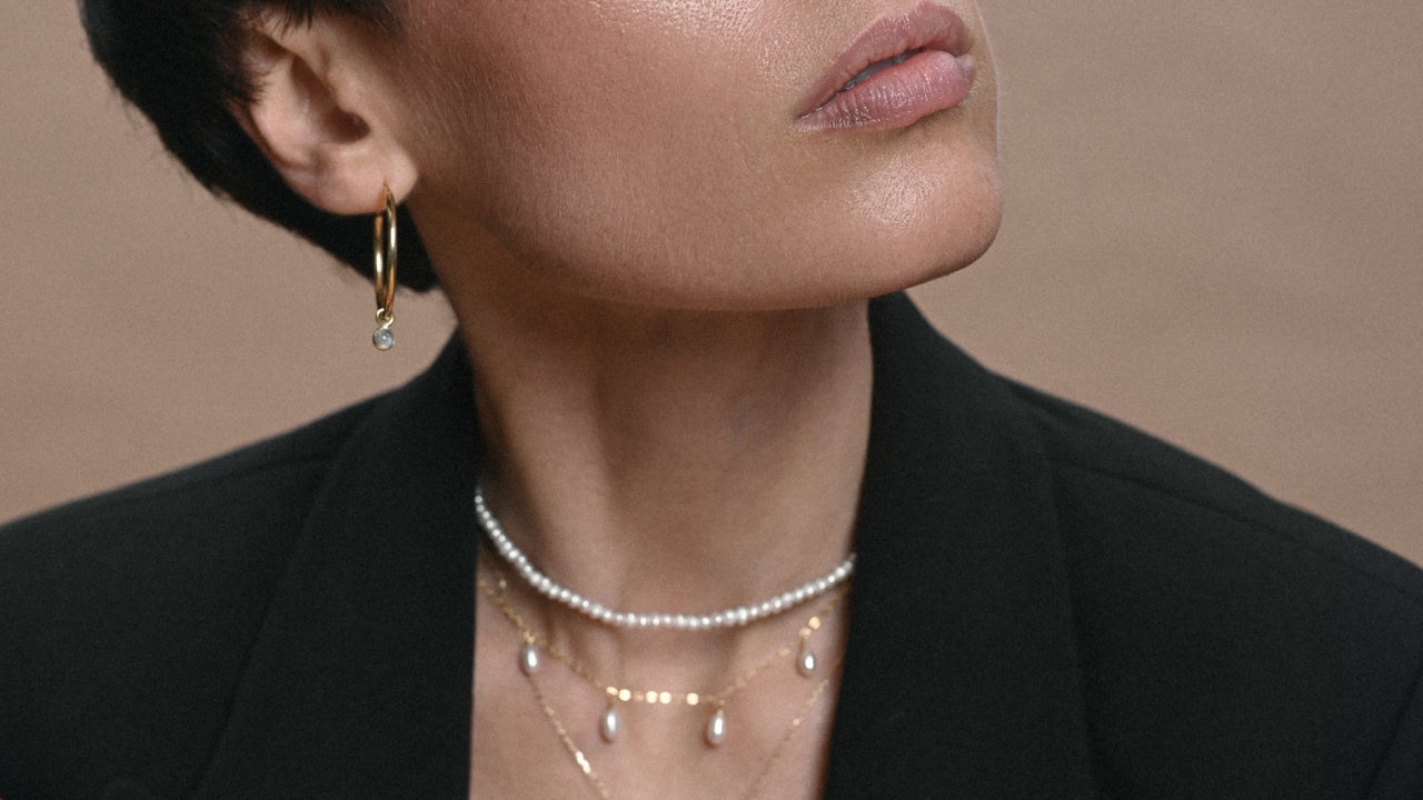 gold hoop earrings with a a precious stone and a layered necklace with pearls and delicate pendants