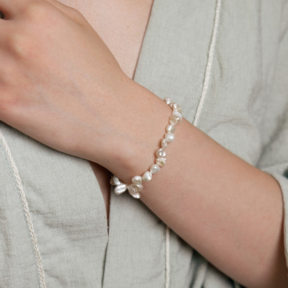 
                      
                        Keshi pearl bracelet on a person's wrist, showcasing its shimmering beauty and icy white hue against a light-colored fabric background.
                      
                    